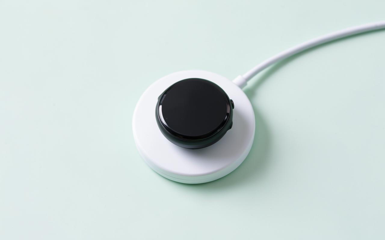 A round smartwatch sitting on a small white magnetic charging puck