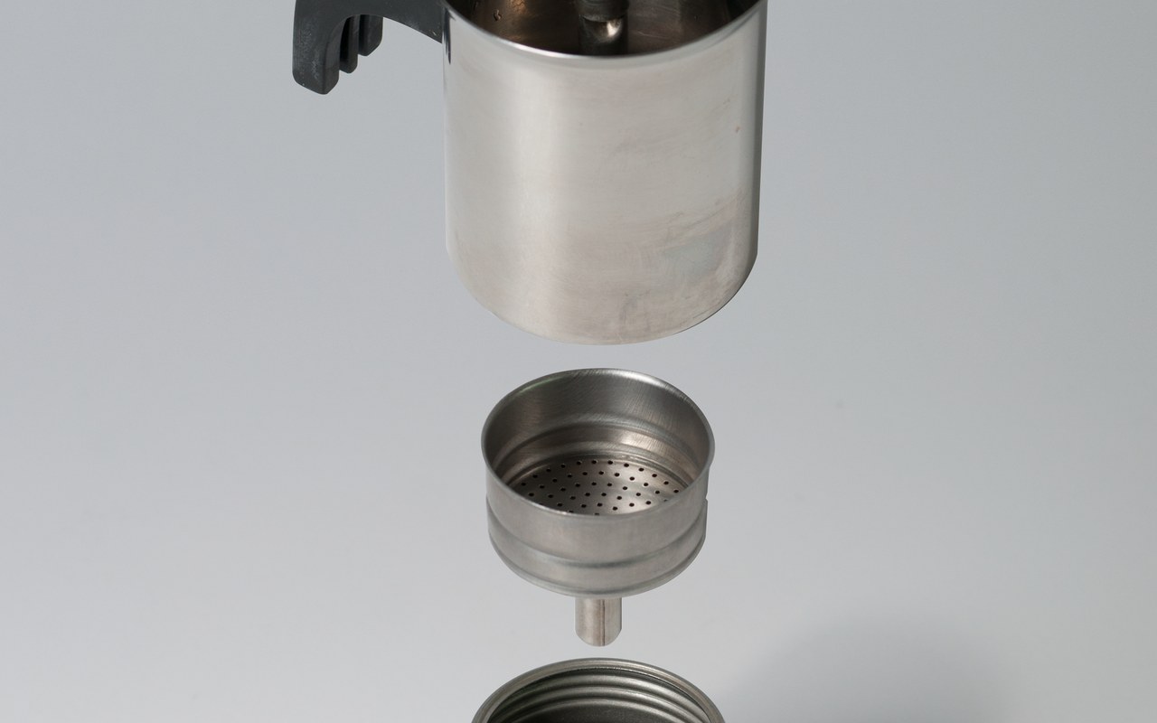 Disassembled moka pot parts floating against a dark background — boiler, funnel, gasket, and upper chamber